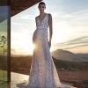 Pronovias Privée Diamond trouwjurk met diepe V-hals en 3D-bloemen, verlicht door een gouden zonsondergang.