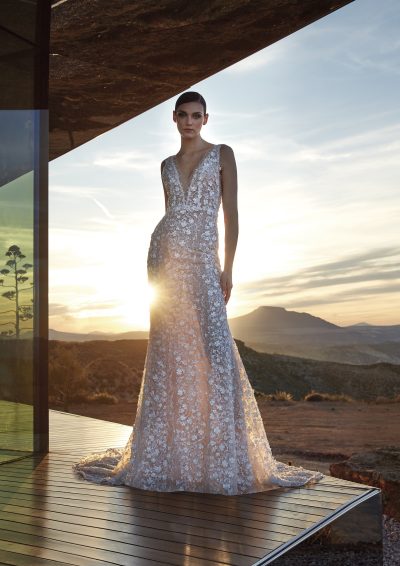 Pronovias Privée Diamond trouwjurk met diepe V-hals en 3D-bloemen, verlicht door een gouden zonsondergang.