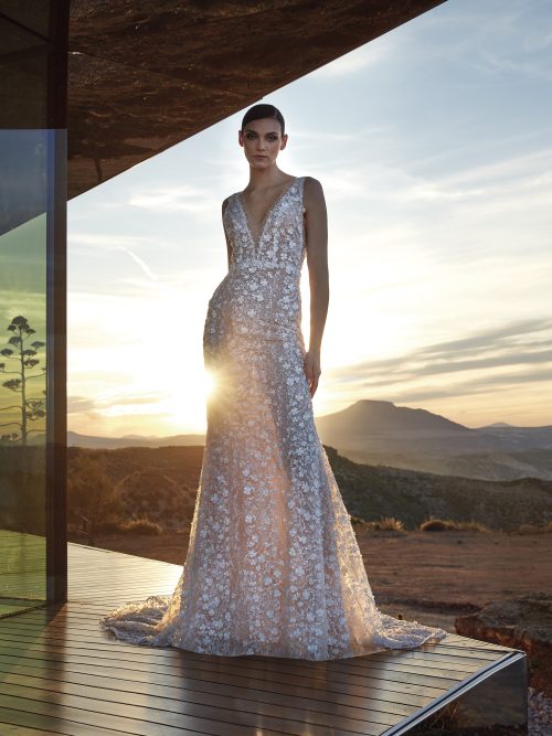 Pronovias Privée Diamond trouwjurk met diepe V-hals en 3D-bloemen, verlicht door een gouden zonsondergang.