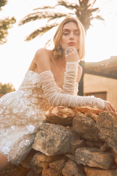 Model poseert in de Pronovias Lulu korte bruidsjurk met doorschijnende lange mouwen.