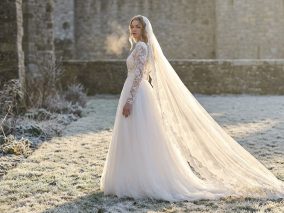 Winter trouwjurk met kanten mouwen en lange sluier in een berijpte kasteeltuin